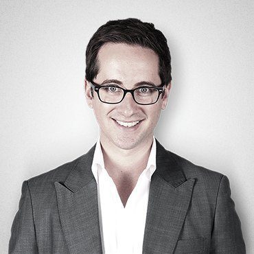 Here's an alt tag for the image: Smiling man in suit and glasses.